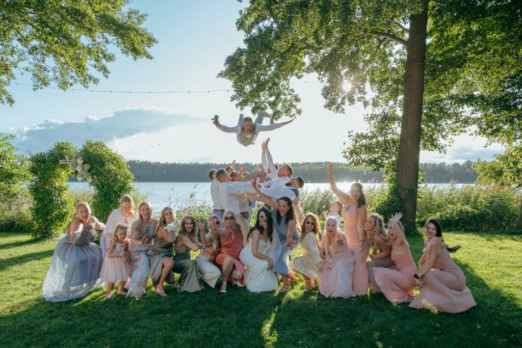 Fröhliche Gruppenaufnahme in der Villa Zesch am See mit Brautpaar und Brautjungfern während einer Sommerhochzeit – inspirierende Hochzeitsfotos für meinen Hochzeitsblog Berlin.