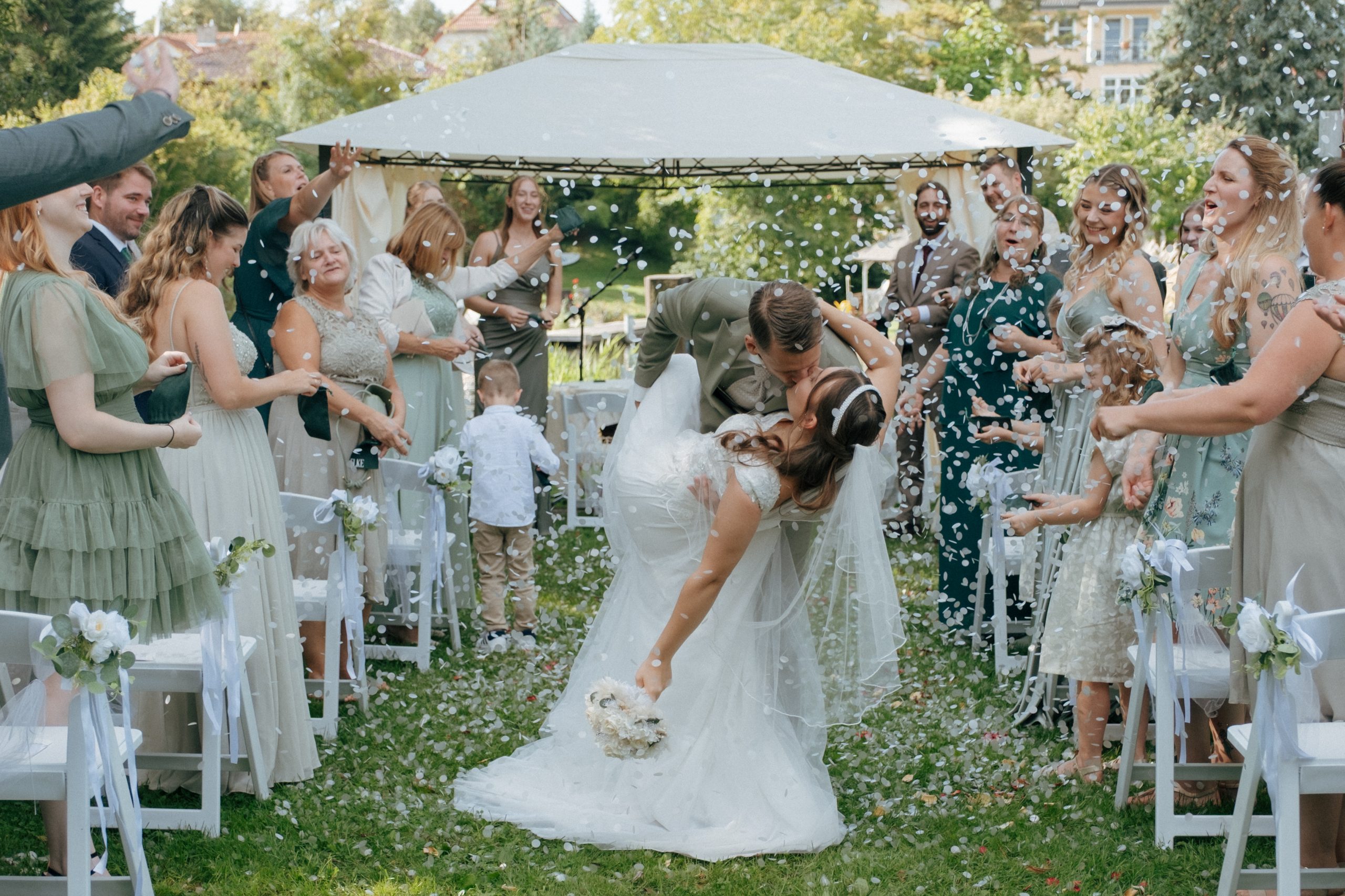 Brautpaar küsst sich beim Auszug nach der freien Trauung, umgeben von jubelnden Gästen und Blütenregen – natürliche Hochzeitsreportage auf meinem Hochzeitsblog Berlin.
